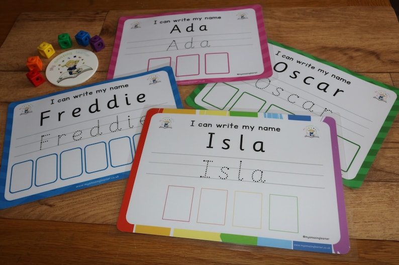 May include: Four colorful laminated cards with dotted lines for tracing letters. Each card has a different name: Ada, Oscar, Isla, and Freddie. The cards are on a wooden surface.