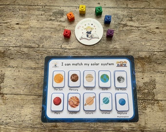 May include: A colorful learning game for kids featuring a blue and white card with images of the planets in our solar system. The card has the text "I can match my solar system". There are also colorful blocks in the image.