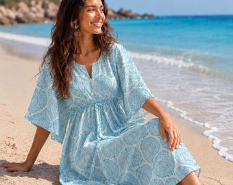 May include: A white midi dress featuring a light blue paisley-inspired circular pattern, a V-neckline, and wide, flowing sleeves. The garment includes a drawstring waist detail and a relaxed, loose-fitting skirt that falls below the knees.