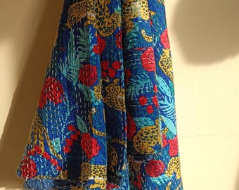 May include: A blue quilt featuring a vibrant pattern of yellow and black leopards, red roses, and green tropical leaves. The fabric is decorated with visible white running stitch embroidery throughout, creating a textured, quilted appearance.