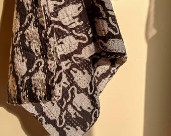 May include: A black and white textile featuring a repeating pattern of stylized animals. The fabric is decorated with visible white running stitch embroidery throughout, creating a textured appearance across the surface of the patterned material.