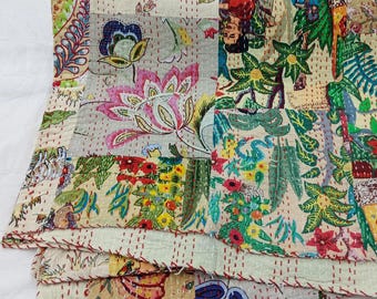 May include: A folded patchwork quilt featuring a variety of colorful floral and botanical patterns in shades of pink, green, yellow, and blue. The fabric is held together by visible red running stitches that create a grid-like texture across the surface.