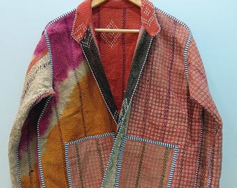 May include: A long-sleeve jacket featuring a patchwork design with various fabric patterns in shades of orange, red, pink, and beige. The garment has a collared neckline, two front pockets, and visible white stitching throughout the fabric.