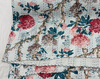 May include: A white cotton quilt featuring a floral pattern with large red and pink peony blossoms, dark teal leaves, and brown branches. The fabric is decorated with rows of straight, dark blue running stitches that create a quilted texture.