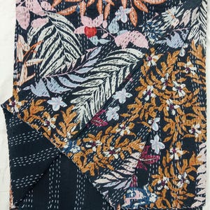 May include: A dark navy blue cotton quilt featuring a dense botanical print of leaves and flowers in shades of orange, light pink, and pale blue. The fabric is detailed with white running stitch kantha embroidery throughout the entire surface.