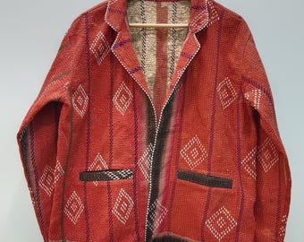 May include: A long-sleeve jacket featuring a vibrant red base with a repeating white diamond pattern and vertical stripes. The garment includes a notched lapel, two front pockets with dark trim, and visible stitching throughout the fabric.