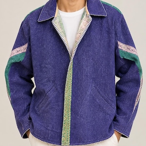May include: A deep blue quilted jacket featuring a collared neckline, long sleeves with green and patterned fabric stripes, and a front opening trimmed with a green floral border. The jacket includes two side pockets and white stitching details.