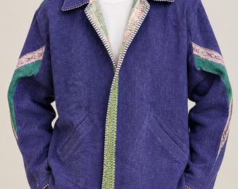 May include: A deep blue quilted jacket featuring a collared neckline, long sleeves with green and patterned fabric stripes, and a front opening trimmed with a green floral border. The jacket includes two side pockets and white stitching details.
