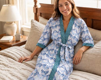 May include: A white robe featuring a repeating blue butterfly pattern, three-quarter length sleeves, and a teal and white striped trim along the front opening and cuffs. The garment includes a matching fabric tie belt at the waist.
