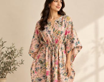 May include: A light pink kaftan dress featuring a vibrant floral pattern in shades of blue, green, and magenta. The garment has a V-neckline, wide kimono-style sleeves, and a drawstring waist tie that creates a gathered silhouette.