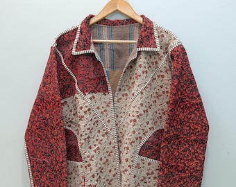 May include: A long-sleeved jacket featuring a patchwork design with alternating panels of deep red textured fabric and a cream-colored fabric with a small red floral pattern. The garment has a collar and visible white stitching along the seams.