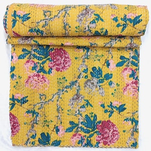 May include: A rolled-up yellow floral quilt with a vibrant design. The quilt features large pink and gray flowers with teal and green leaves and stems. The quilt is made of a soft material and is stitched with white thread.