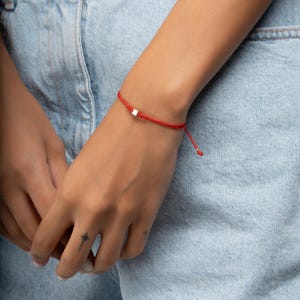 May include: A red string bracelet with a small silver square charm.