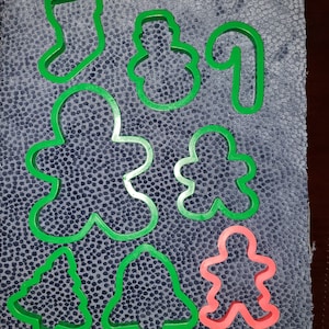 Puede incluir: Un conjunto de nueve cortadores de galletas de plástico verde y rojo con forma de calcetín, muñeco de nieve, bastón de caramelo, hombre de jengibre, persona de jengibre, campana, árbol de Navidad y una persona de jengibre.