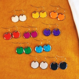 May include: Assortment of colorful round earrings with gold hooks. The earrings are made of resin and have a variety of colors, including red, blue, green, yellow, and white.