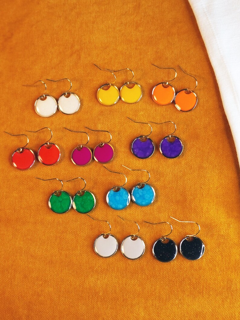 May include: Assortment of colorful round earrings with gold hooks. The earrings are made of resin and have a variety of colors, including red, blue, green, yellow, and white.