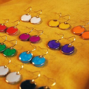 May include: A set of 10 pairs of colorful round earrings with gold hooks. The earrings are made of enamel and come in a variety of colors, including red, green, blue, purple, yellow, and orange.