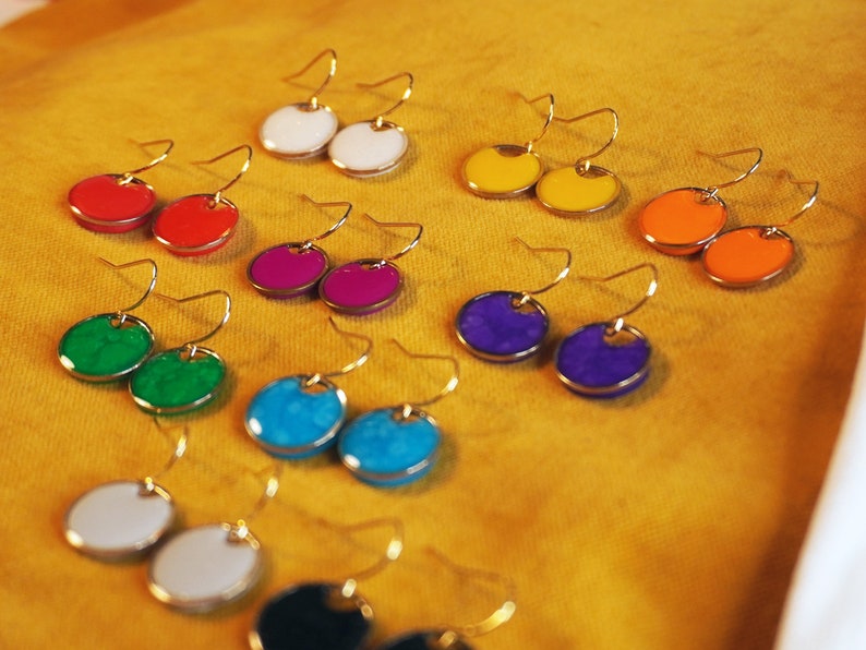 May include: A set of 10 pairs of colorful round earrings with gold hooks. The earrings are made of enamel and come in a variety of colors, including red, green, blue, purple, yellow, and orange.