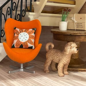 May include: A miniature interior scene featuring an orange chair with a floral cushion. A small brown dog figurine stands nearby. A round table holds a plant and a wrapped parcel. The chair is reminiscent of mid-century modern design.