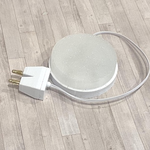 May include: A white, round, frosted glass light fixture with a white base and a white power cord. The fixture is connected to a white electrical plug with two prongs.