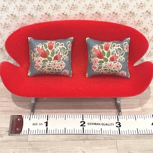 Peut inclure: Un petit canapé rouge avec deux coussins décoratifs. Les coussins sont bleus avec un motif floral de fleurs roses et vertes. Le canapé mesure environ 7,6 cm de large.
