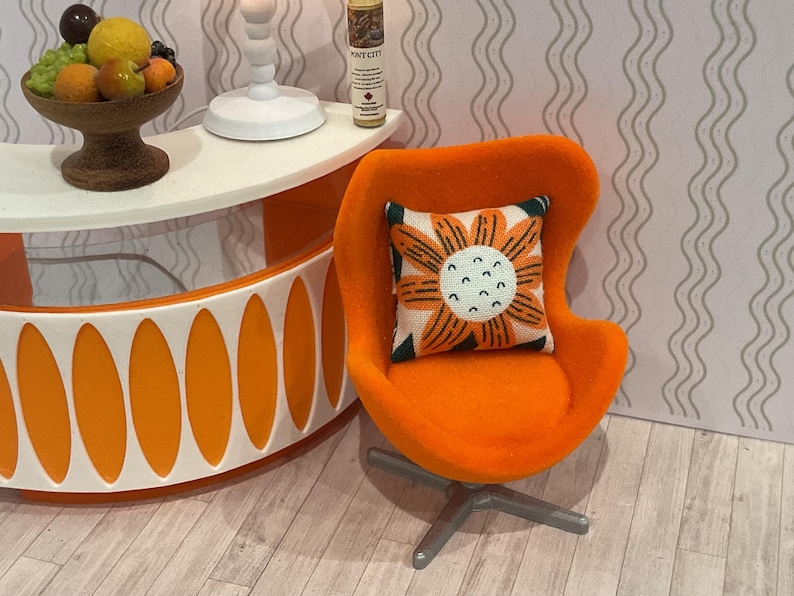 May include: An orange mid-century modern style chair with a floral pillow. The pillow has a white background with an orange flower design. The chair sits on a silver base. A white and orange table is in the background.