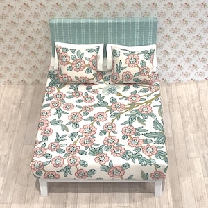 May include: A miniature bed with a light blue headboard and white legs. The bedding features a floral pattern with pink flowers and green leaves on a white background. Two matching pillows are on the bed.