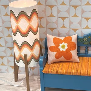 May include: A retro-style floor lamp with a wavy pattern in shades of orange, brown, and white. The lamp is next to a blue bench with an orange cushion and a flower-shaped pillow. The background features a geometric pattern.