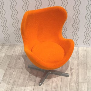 May include: An orange, mid-century modern style chair with a rounded back and seat. The chair has a swivel base with a dark gray finish. The chair is made of a textured, orange fabric.
