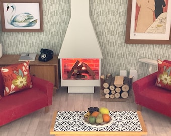 May include: A miniature living room scene featuring a white fireplace with glowing logs, two red sofas with floral pillows, a wooden coffee table with a bowl of fruit, a black rotary telephone, and framed wall art including a swan illustration.