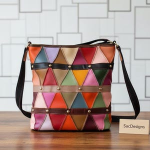 Könnte beinhalten: Eine mehrfarbige Umhängetasche mit einem geometrischen Patchwork-Muster aus dreieckigen Lederfeldern in Rot, Orange, Gelb, Grün, Blau, Rosa und Braun, akzentuiert durch drei horizontale dunkelbraune Lederriemen mit goldfarbenen Nieten.