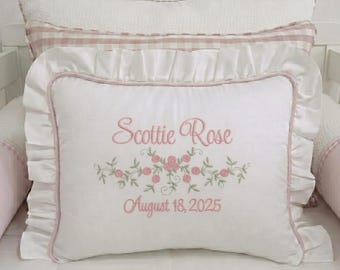 May include: A white rectangular throw pillow with a ruffled border and pink piping. The center features pink embroidered text reading Scottie Rose, a floral vine motif with pink roses and green leaves, and the date August 18, 2025 in pink text.
