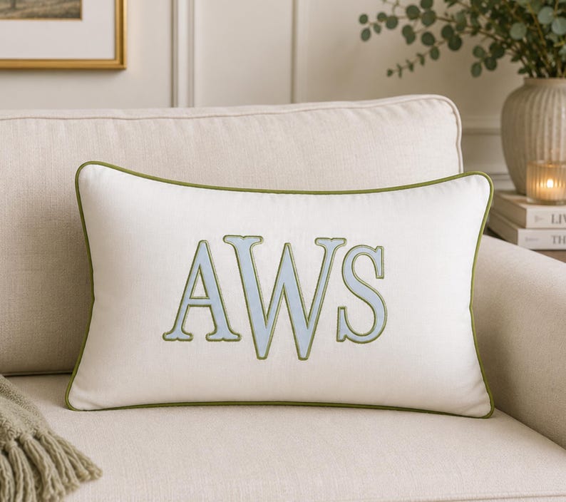May include: A rectangular off-white throw pillow featuring the embroidered letters AWS in light blue with a sage green outline. The pillow is finished with matching sage green piping along all four edges, creating a clean and structured appearance.