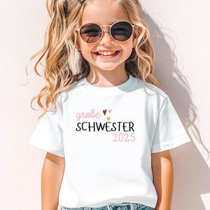 personalisiertes weißes t-shirt mit dem text große schwester 2025, mit boho herz Motiv. t-shirt zur schwangerschaft verkünden.
