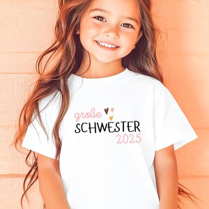 personalisiertes weißes t-shirt mit dem text große schwester 2025, mit boho herz Motiv. t-shirt zur schwangerschaft verkünden.