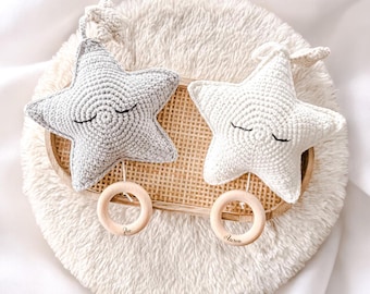 Puede incluir: Dos adornos de ganchillo en forma de estrella, uno gris claro y otro blanco roto, cada uno con ojos cerrados bordados. Cada estrella está unida a un pequeño anillo de madera clara, con los nombres Zoe y Aaron grabados en los anillos.