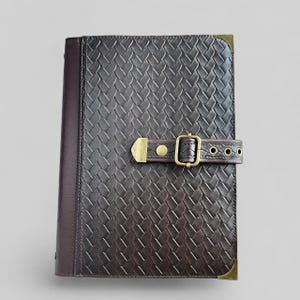 May include: A brown leather journal with a woven pattern and a brass buckle closure.