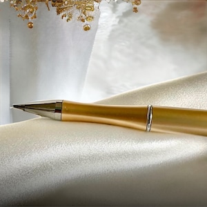 May include: A gold pen with a silver band on a white satin background.
