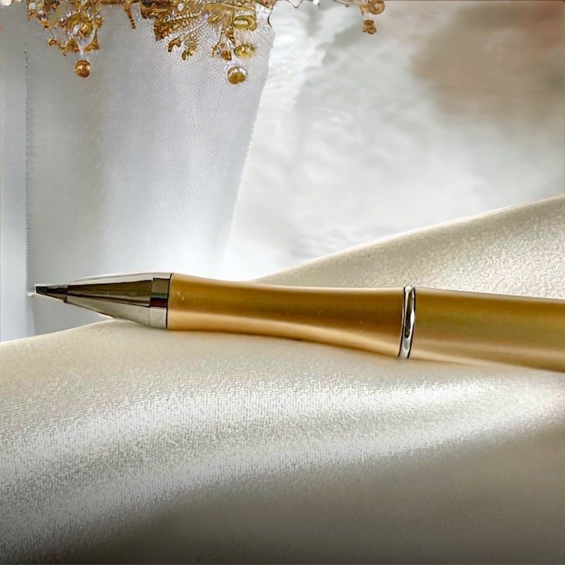 May include: A gold pen with a silver band on a white satin background.