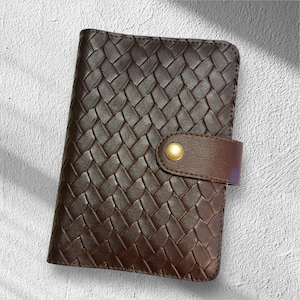 May include: A brown leather wallet with a woven pattern. The wallet has a flap closure with a gold-colored button. The leather is a rich, dark brown color. The wallet is rectangular in shape.