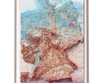 May include: A framed physical relief map of Germany featuring a 3D-style topographical rendering. The map displays varied terrain in shades of deep red, brown, and blue, with detailed geographical markings, a legend, and text labels in a light wood frame.