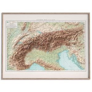 May include: A framed vintage map titled "General Map of the Alps." The map shows a detailed, three-dimensional rendering of the Alps mountain range, with shades of brown, green, and blue. The frame is a light wood colour.