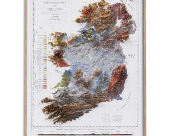 Può includere: Mappa geologica incorniciata dell'Irlanda, che mostra un modello in rilievo dettagliato con colori vari che rappresentano diverse caratteristiche geologiche. La mappa include testo che indica la scala e il titolo, incorniciata in legno chiaro.