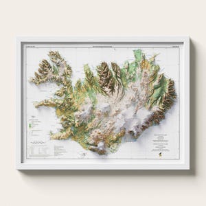 May include: A framed topographic map of Iceland featuring a white background with detailed 3D-style relief shading. The map displays green, brown, and white terrain textures, grid lines, a legend, and text including "NATTURUFRAEDISTOFNUN ISLANDS".