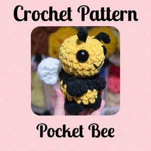 Puede incluir: Patrón de crochet para un amigurumi abeja de bolsillo. La abeja es amarilla y negra con grandes ojos negros y una boca sonriente. El patrón se llama "Pocket Bee".