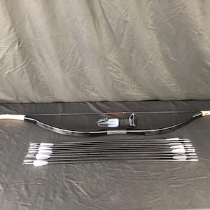 May include: A black recurve bow with white tips and a black leather grip. The bow is accompanied by a set of 10 black arrows with white fletching.