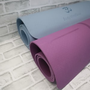 May include: Two yoga mats rolled up, one is light blue with the text "Body Mind Soul" and an Om symbol, the other is purple with an Om symbol.