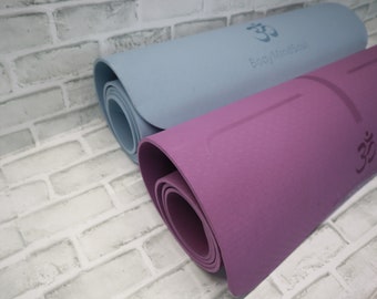 May include: Two yoga mats rolled up, one is light blue with the text "Body Mind Soul" and an Om symbol, the other is purple with an Om symbol.