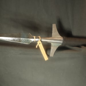 Peut inclure: Une lance avec une lame en m&eacute;tal poli et un manche en bois. La lame est fix&eacute;e &agrave; une garde transversale en m&eacute;tal. La tige est envelopp&eacute;e d'un mat&eacute;riau noir pr&egrave;s de la lame. Une petite &eacute;tiquette est attach&eacute;e &agrave; la lance.