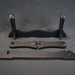 May include: A black wooden sword stand with three pieces. The stand is designed to hold two swords. The stand is made of wood and has a simple design.